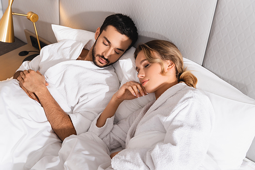 High angle view of interracial couple in bathrobes sleeping in hotel room