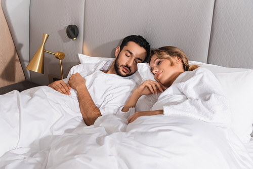 Young interracial couple sleeping on white bedding in hotel