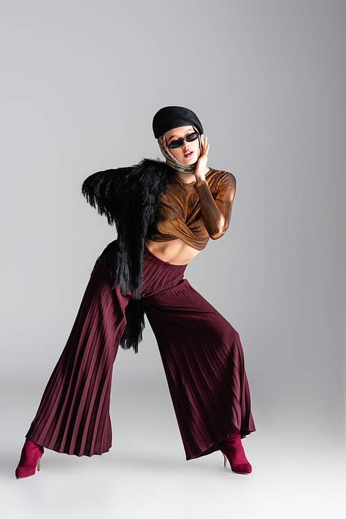 full length of woman in stylish sunglasses and beret posing on grey