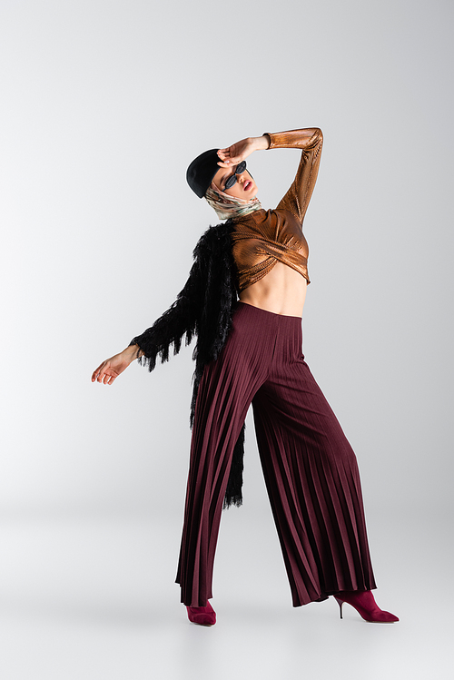 full length of young woman in trendy sunglasses and beret posing on grey