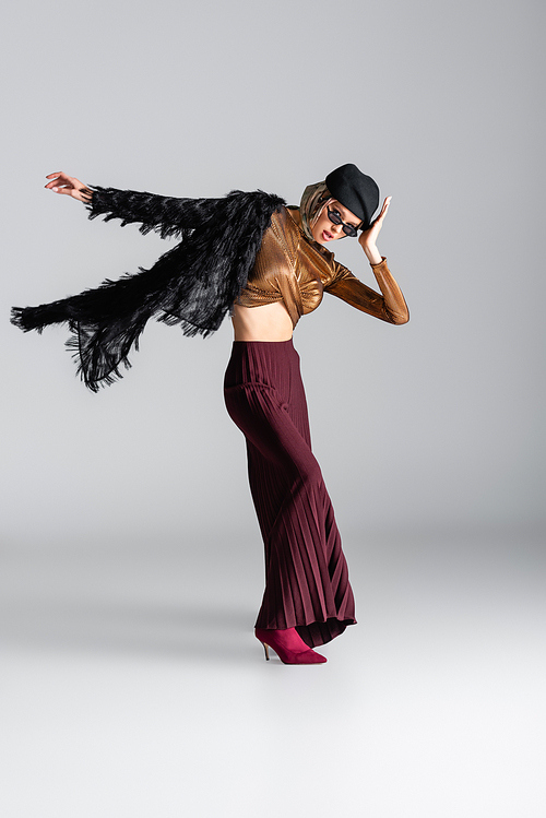 full length of fashionable woman in sunglasses and beret posing on grey