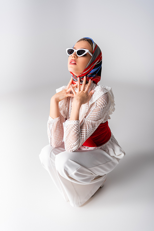 stylish woman in headscarf and sunglasses sitting on white