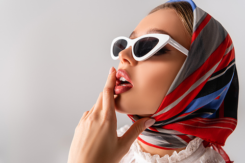 young and sensual woman in headscarf and sunglasses touching lips isolated on white