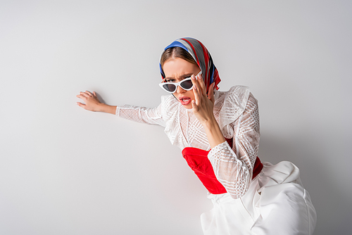 high angle view of young trendy woman in headscarf touching sunglasses on white