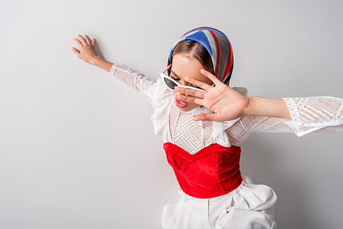 high angle view of young trendy woman in headscarf and sunglasses gesturing on white