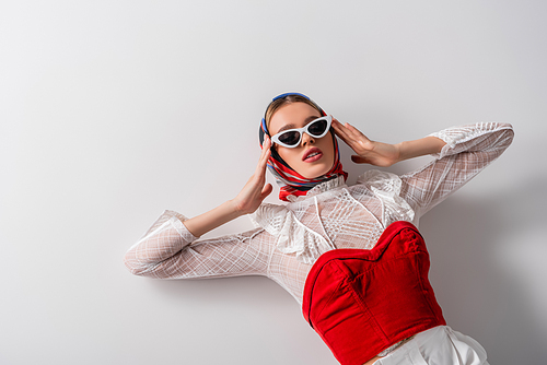 high angle view of young trendy woman in headscarf and sunglasses lying on white