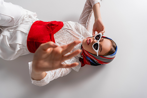 top view of trendy woman in headscarf and sunglasses lying with outstretched hand on white