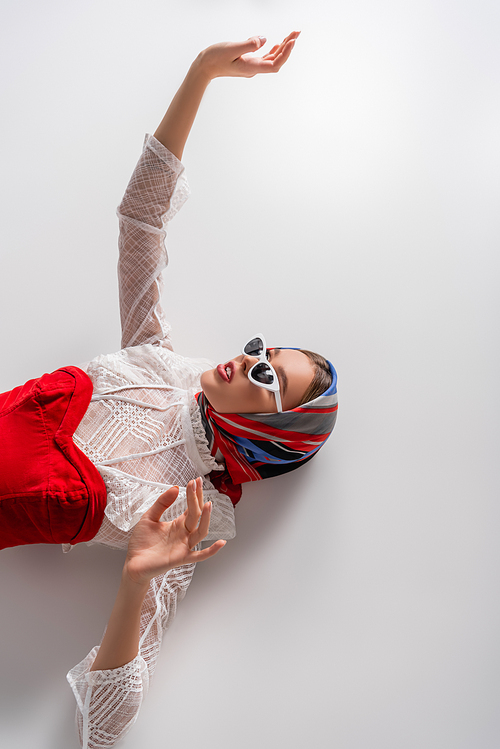 top view of stylish woman in headscarf and sunglasses lying with outstretched hand on white