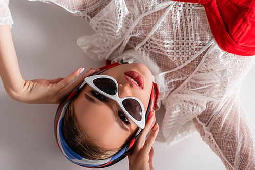 top view of trendy woman in sunglasses and headscarf lying while  on white