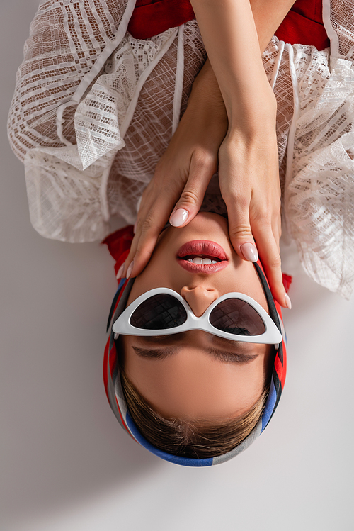 top view of stylish woman in sunglasses and headscarf lying while  on white