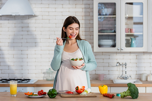 joyful pregnant woman eating fresh vegetable salad for breakfast