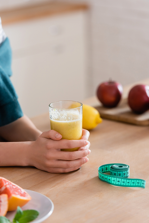 partial view of woman near glass of fruit juice and measuring tape, blurred background