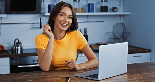 happy woman using laptop and holding credit card while online shopping