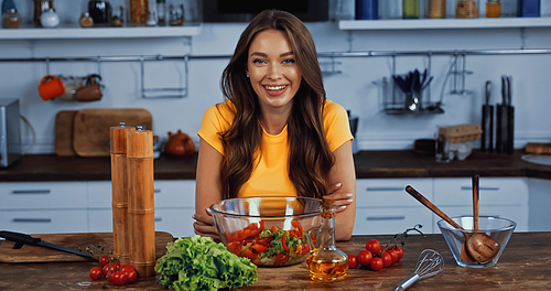 happy young woman smiling near bowl with fresh mixed salad