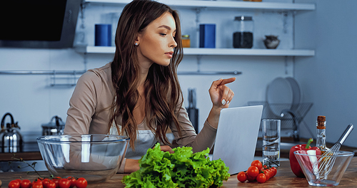 young woman pointing with finger near laptop and ingredients on table