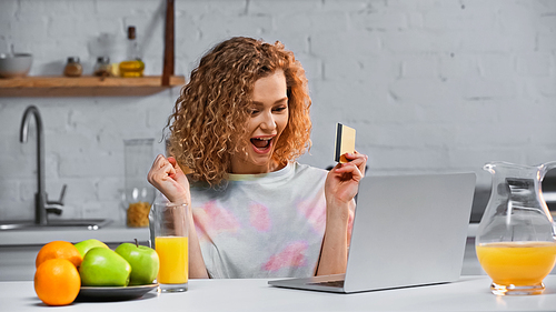 excited young woman holding credit card while shopping online in kitchen