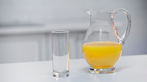 jug with fresh orange juice near glass on kitchen table