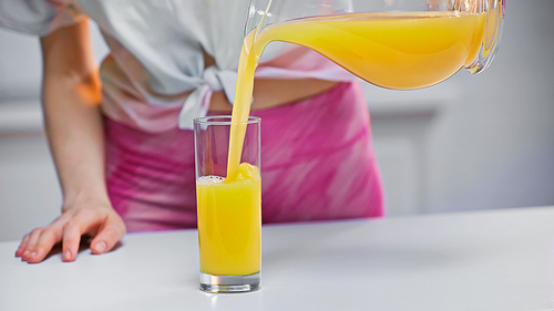 cropped view of woman pouring fresh orange juice in glass