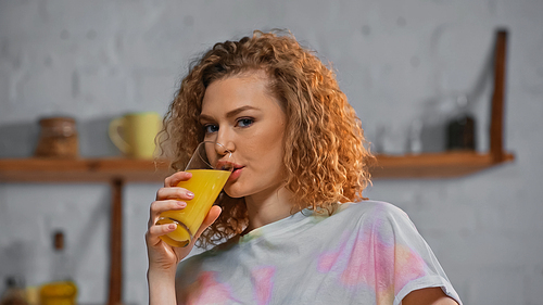curly woman  while drinking orange juice in kitchen