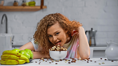 curly woman eating pile of corn flakes in bowl