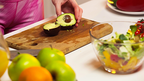 cropped view of woman near avocado halves on chopping board