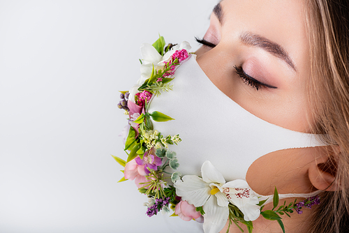 Woman with closed eyes wearing medical mask with flowers and leaves isolated on grey