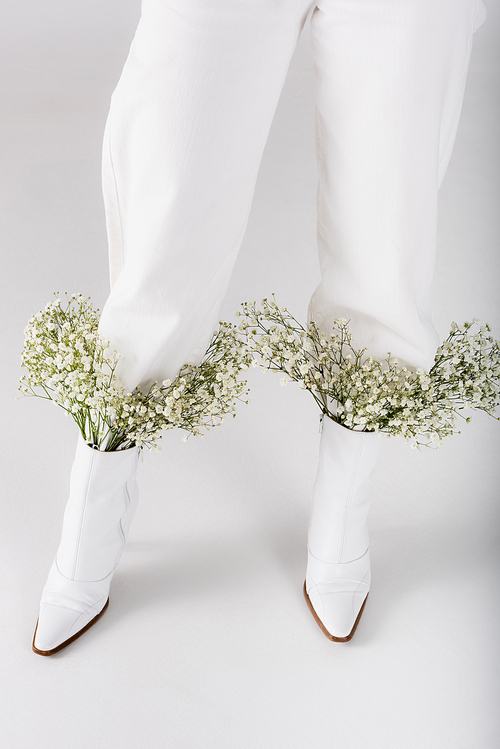 Cropped view of baby breath flowers in shoes of woman on grey background