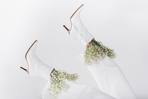 Partial view of small white flowers in shoes of woman isolated on grey