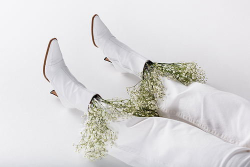 Cropped view of legs of woman in white shoes and pants with flowers on grey background