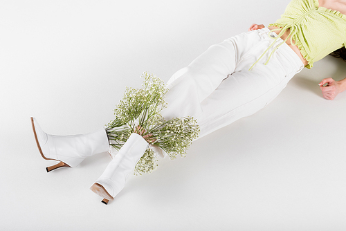 Cropped view of stylish woman with flowers in shoes lying on grey background