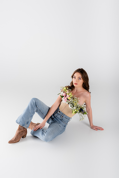 Brunette woman with flowers in blouse  while sitting on grey background