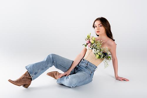 Young stylish model with flowers in blouse sitting on grey background