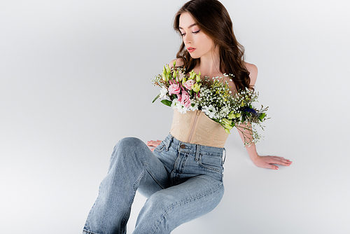 Woman in jeans and blouse with flowers sitting isolated on grey