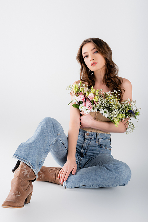 Fashionable model with flowers in blouse  while sitting on grey background