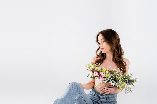 Curly woman with different flowers in blouse looking at jeans isolated on grey