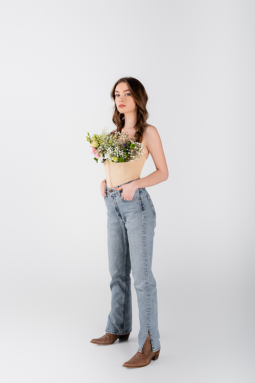 Young model with flowers in blouse and hands in pockets of jeans  on grey background