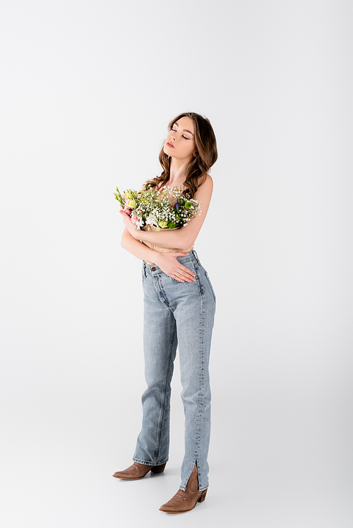 Brunette model with flowers in blouse standing with closed eyes on grey background