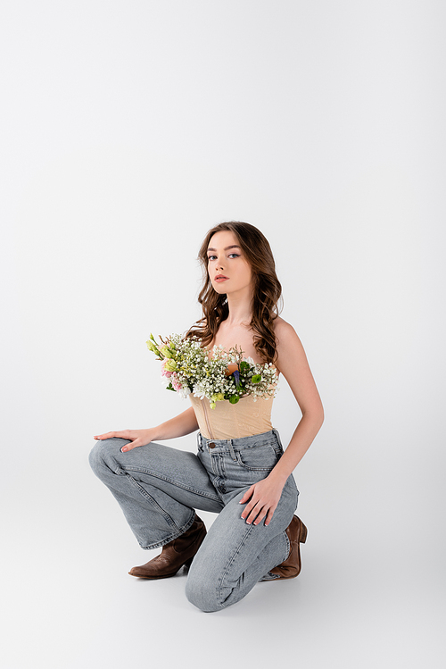 Stylish young model with bouquet in blouse posing on grey background