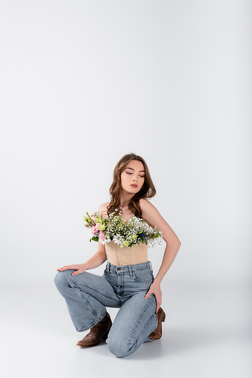 Young model with flowers in blouse kneeling on grey background