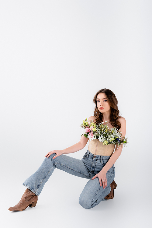 Young model in jeans, shoes and flowers in blouse on grey background