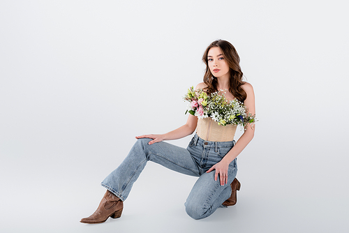 Brunette woman in brown shoes, jeans and flowers in blouse on grey background
