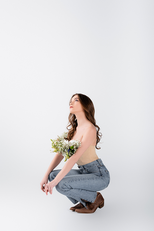 Stylish woman with flowers in blouse looking up on grey background
