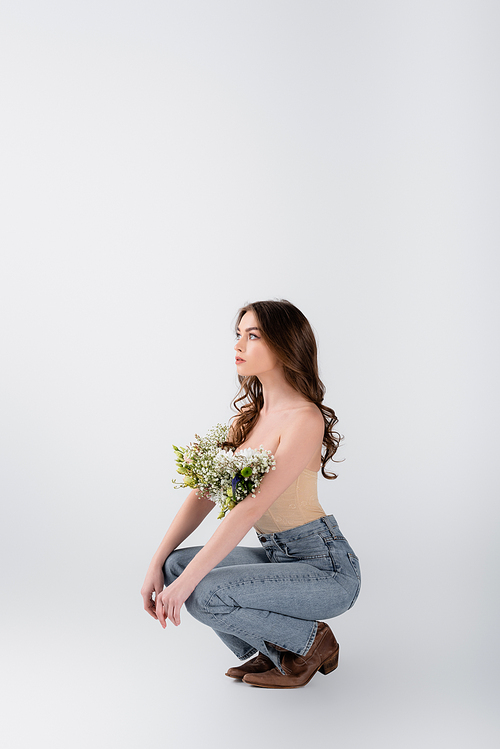 Young woman with naked shoulders and flowers in blouse looking away on grey background