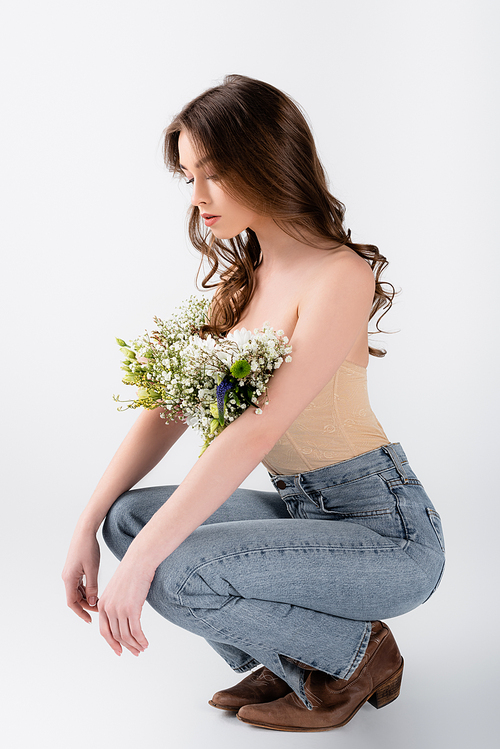 Curly model looking at flowers in blouse on grey background