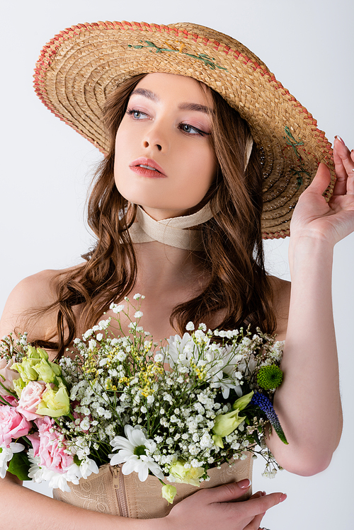 Young model in straw hat and different flowers in blouse isolated on grey