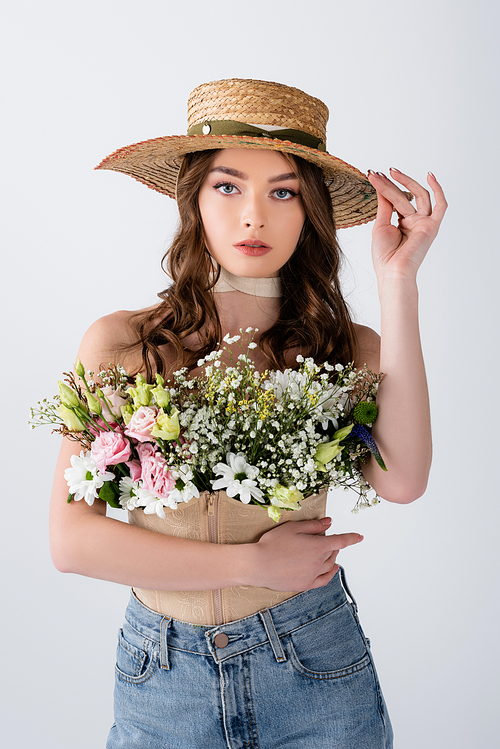 Brunette model holding sun hat and flowers in blouse isolated on grey