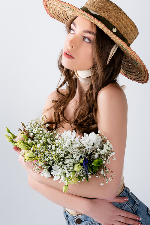 Young woman in stylish straw hat holding flowers isolated on grey