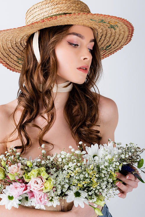 Young model in sun hat holding flowers isolated on grey