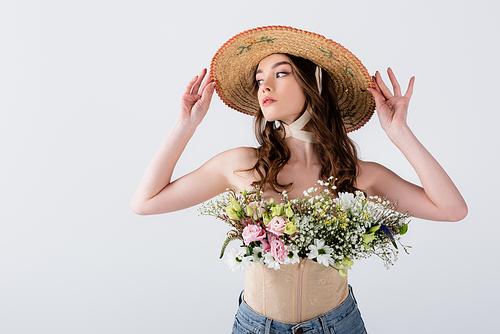 Young woman posing with straw hat and flowers isolated on grey