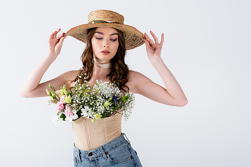 Trendy woman holding sun hat and posing with different flowers in blouse isolated on grey